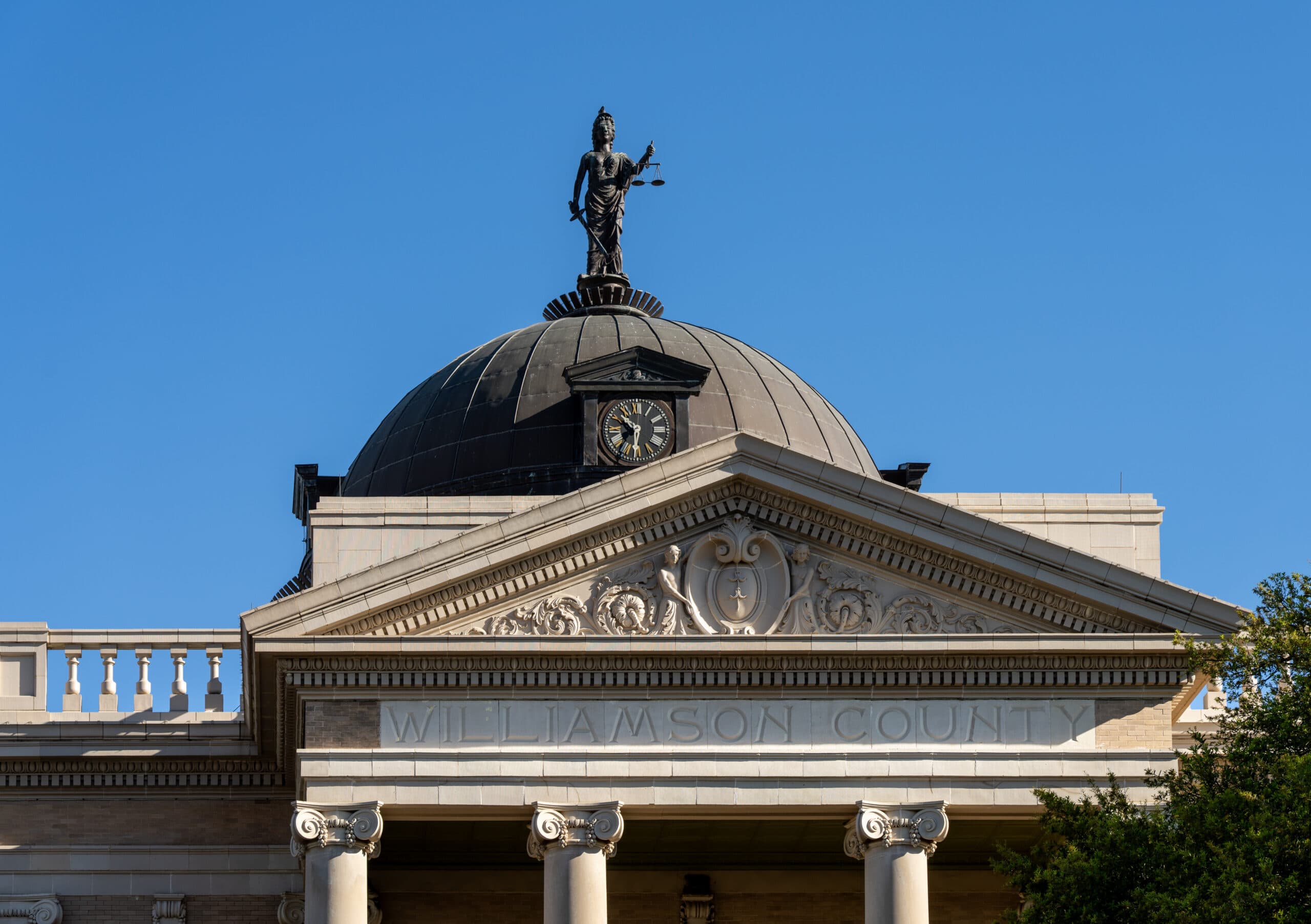 A historic courthouse in Georgetown, Texas features a statue on its dome against a clear blue sky.